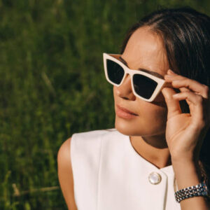A young woman in sunglasses with a white frame on a summer green background