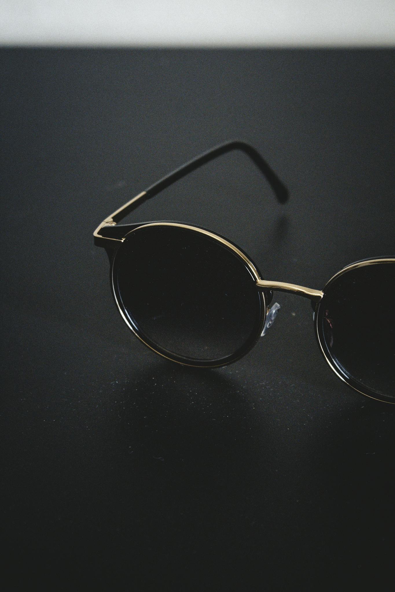 Close-up of round sunglasses with gold frame on a dark surface, emphasizing minimalist style.